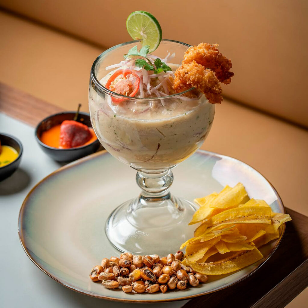 Leche de tigre servida en una copa, acompañada de chicharrón de calamar y chifles