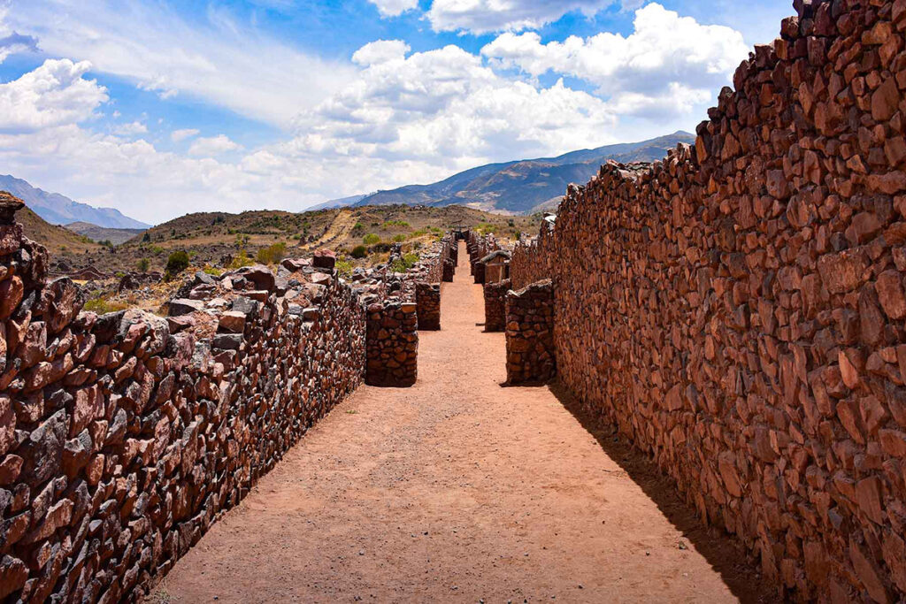 Vista de los muros de piedra en Pikillaqta, Cusco, con pasadizos alineados y montañas al fondo
