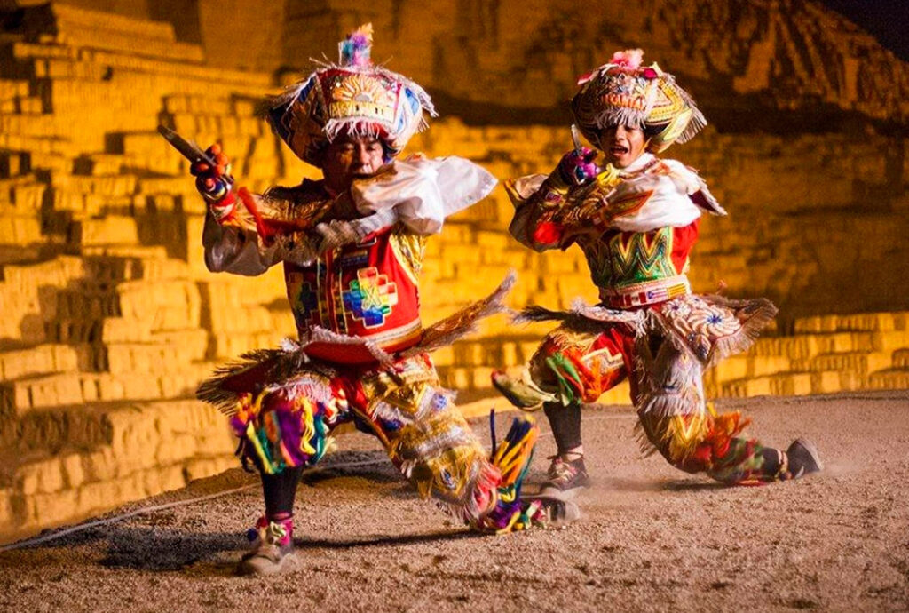 Dúo de danzantes de tijeras vestidos con trajes típicos intepretando la danza de las tijeras en un piso de tierra