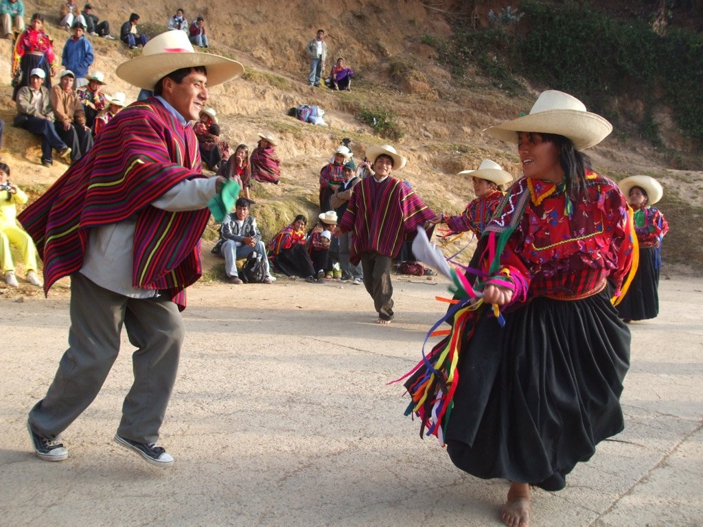 Hombre vestido con poncho y sombrero baila huayno con una mujer vestida de traje típico, listones y sombrero