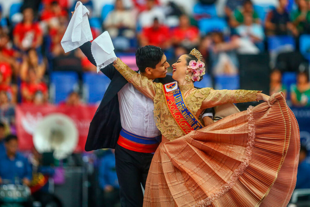 Pareja de bailarines de marinera peruana durante una competencia en Trujillo, vistiendo trajes tradicionales y agitando pañuelos al ritmo de la música criolla