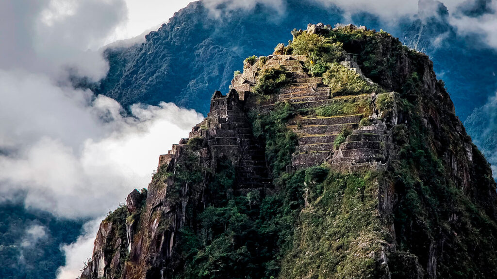 Vista del Huayna Picchu con estructuras incas en sus laderas, rodeado de nubes y vegetación andina