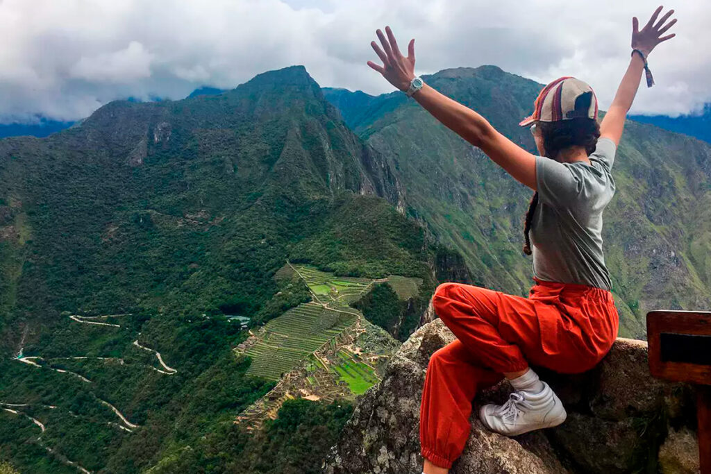 Mujer con los brazos extendidos celebra su ascenso, contemplando Machu Picchu desde la cima del Huayna Picchu