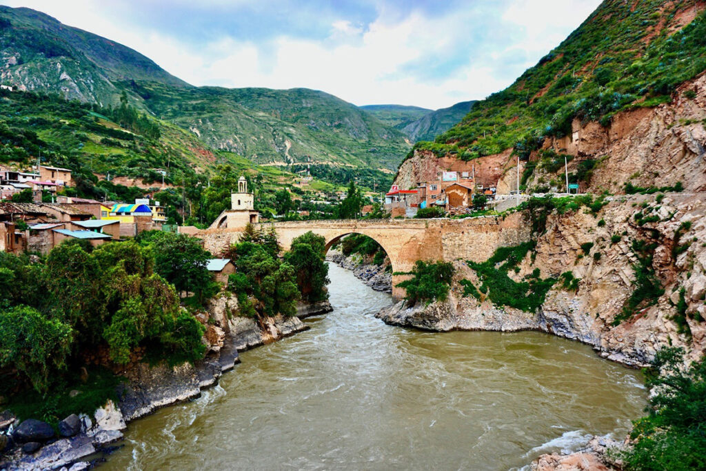 Puente colonial de Izcuchaca sobre el río Mantaro, rodeado de montañas y arquitectura tradicional andina.
