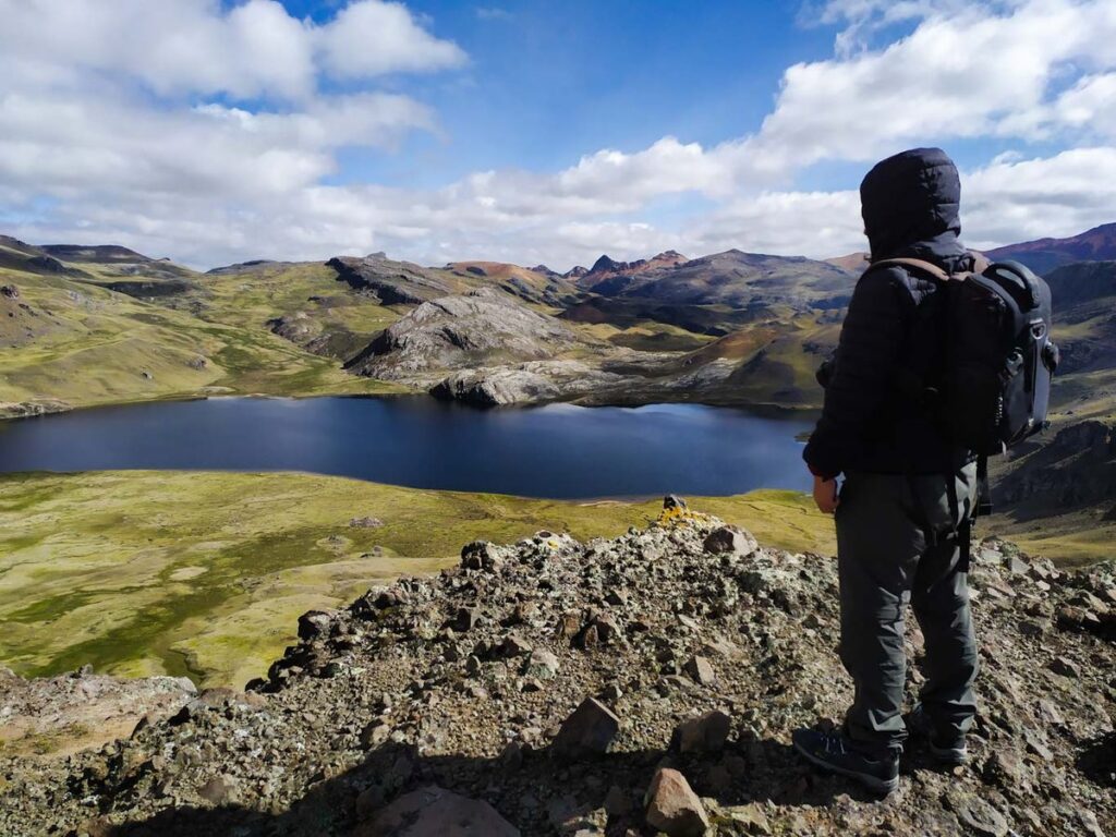 Excursionista observa una laguna altoandina en Huancavelica desde un mirador natural, rodeado de montañas.