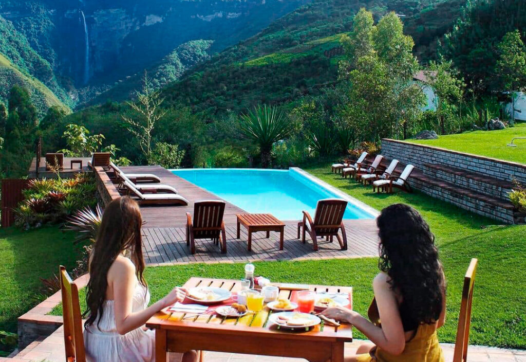 Turistas desayunan junto a una piscina con vista a las Cataratas de Gocta desde un hospedaje rural en Cocachimba, región Amazonas, Perú
