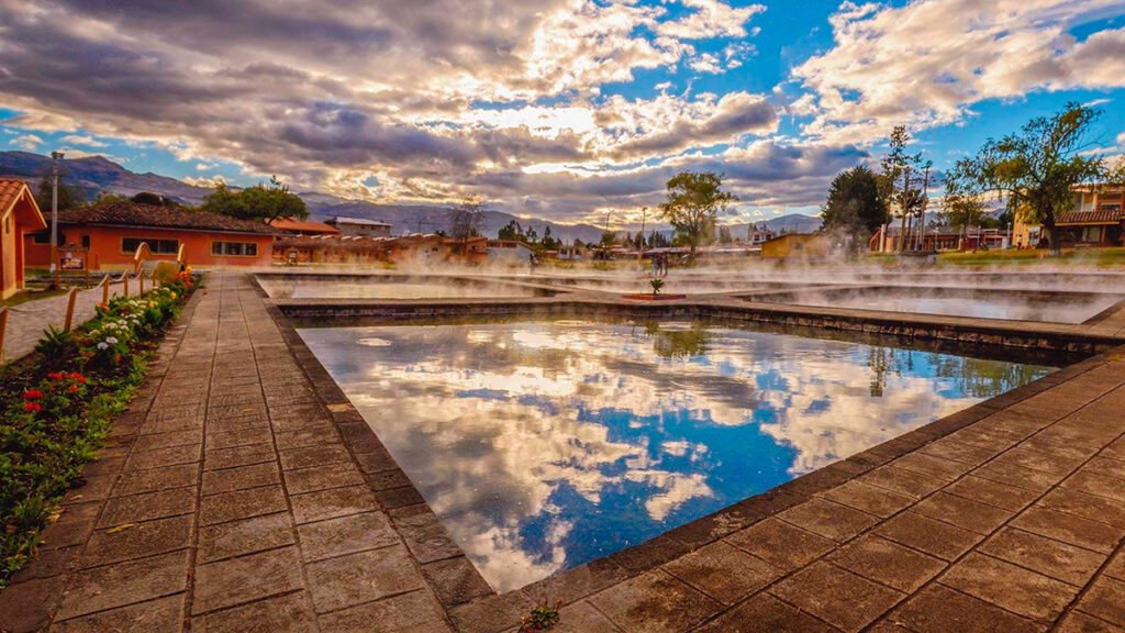 Vista panorámica del complejo turístico Baños del Inca al amanecer, con vapor natural y cielo reflejado en las piscinas termales