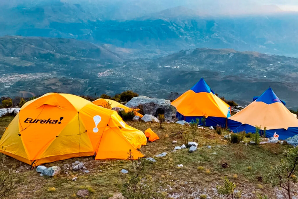 Campamento con carpas naranjas instalado en una ladera andina cerca del Nevado Huascarán