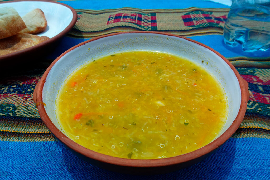 sopa de quinua andina servida en un mantel con diseños andinos, acompañada de pan