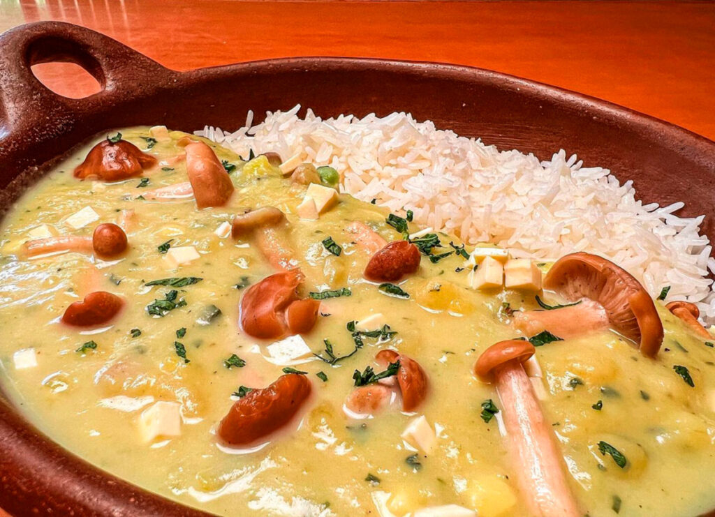 Plato hondo con kapchi de habas, un guiso andino cremoso a base de habas frescas, queso y ají, servido con papas y arroz