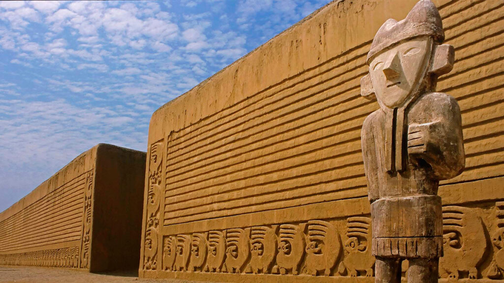 Escultura chimú en la entrada de la ciudadela de Chan chan, rodeada de muros de adobe decorados con frisos geométricos y figuras mitológicas, en Trujillo, Perú