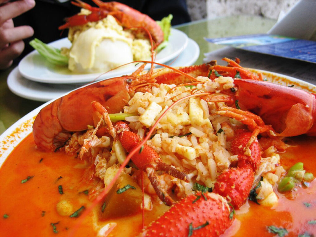 Plato de chupe de camarones arequipeño, servido en fuente honda con camarones de río, arroz, hierbas y caldo espeso, acompañado de guarnición al fondo
