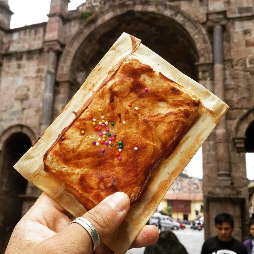 Empanada dulce cusqueña en la mano de un turista mientras camina por las calles de Cusco