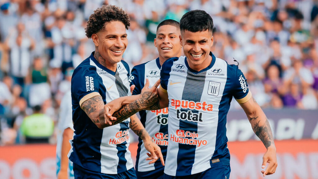 Futbolistas de Alianza Lima sonrientes tras una jugada, con camiseta blanquiazul y tribuna de fondo durante un encuentro oficial.