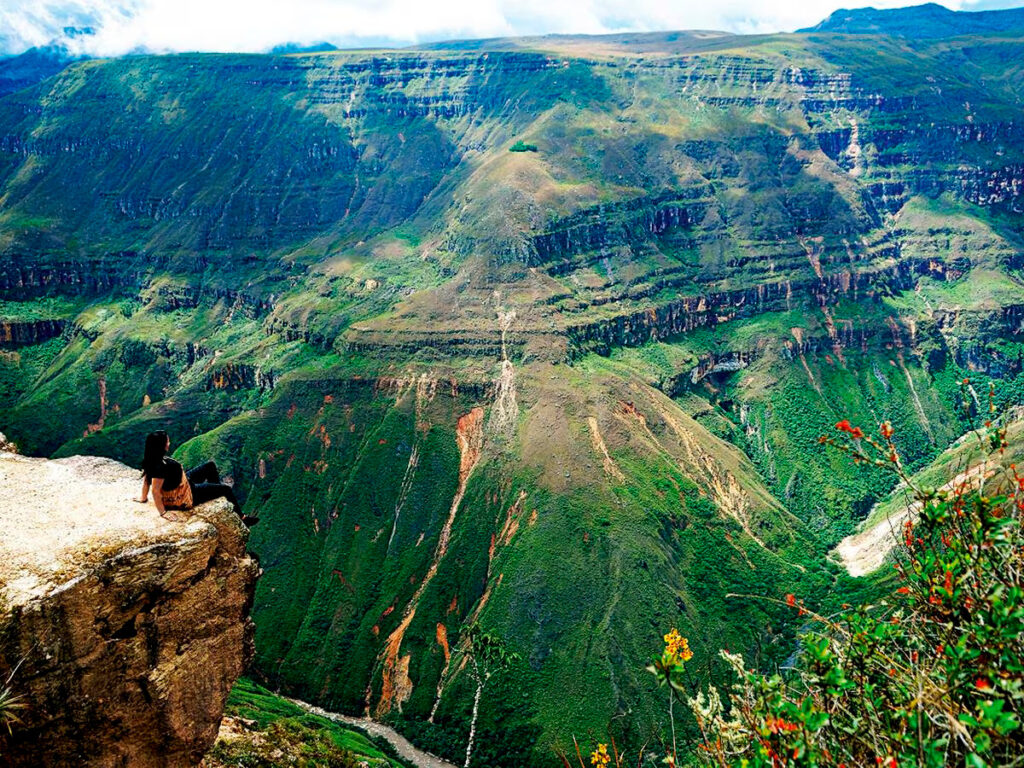 Panorámica del Cañón del sonche con una persona sentada al borde del mirador natural, rodeado de laderas verdes