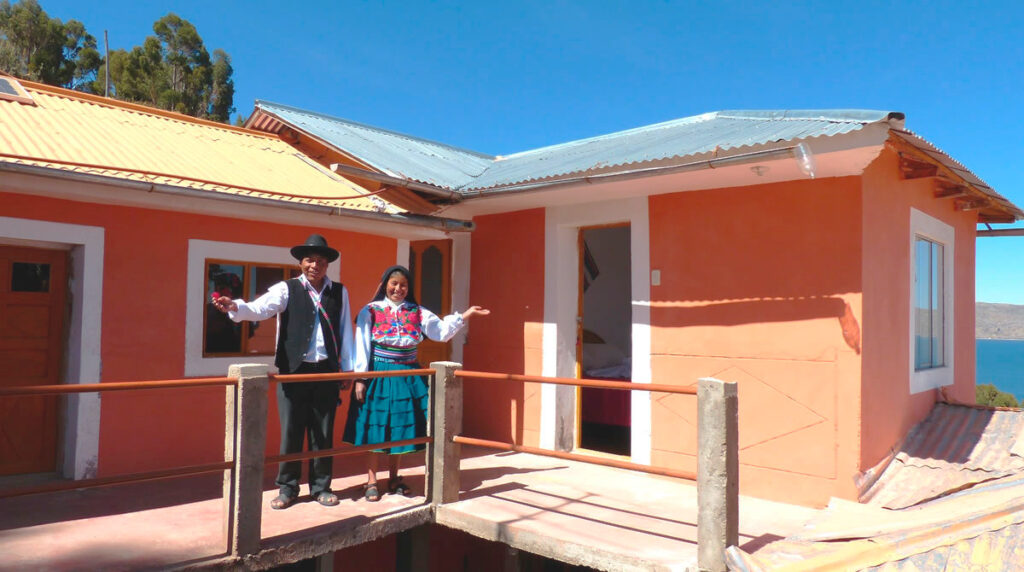 Pareja de la comunidad de Amantaní con vestimenta tradicional, recibiendo a los visitantes frente a su hospedaje rural de adobe y techos metalizados