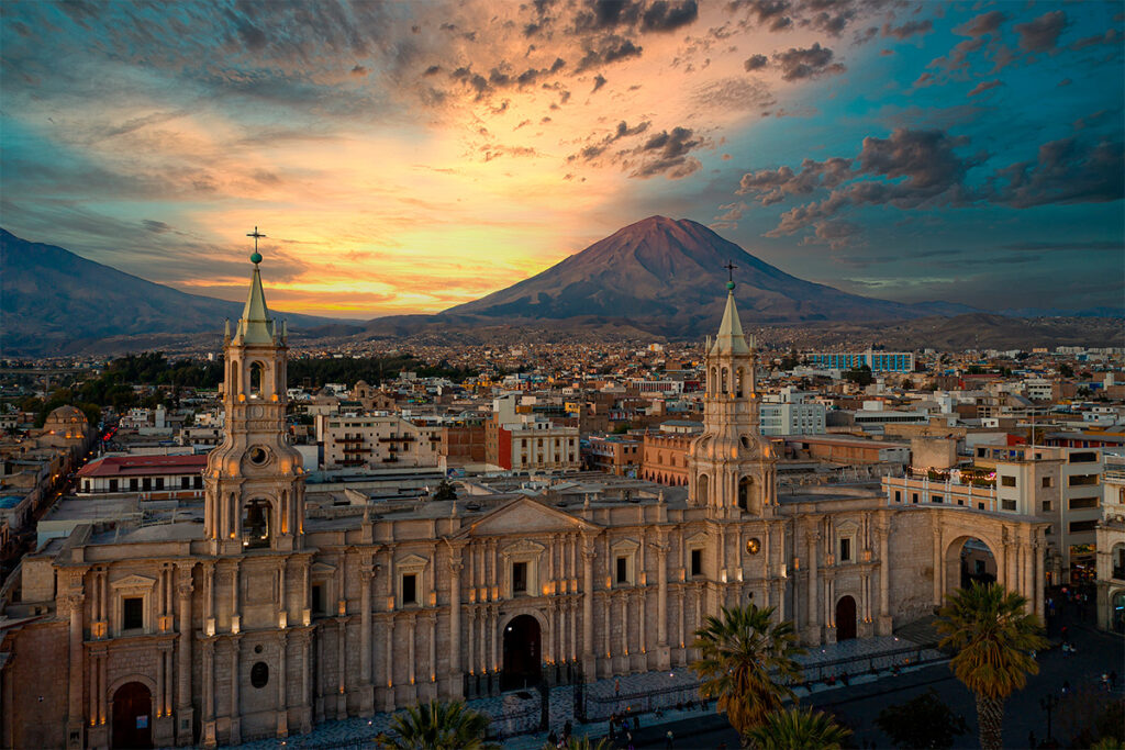 Vista de la Catedral de Arequipa al atardecer con el volcán Misti al fondo y cielo dramático sobre el centro histórico de la ciudad.