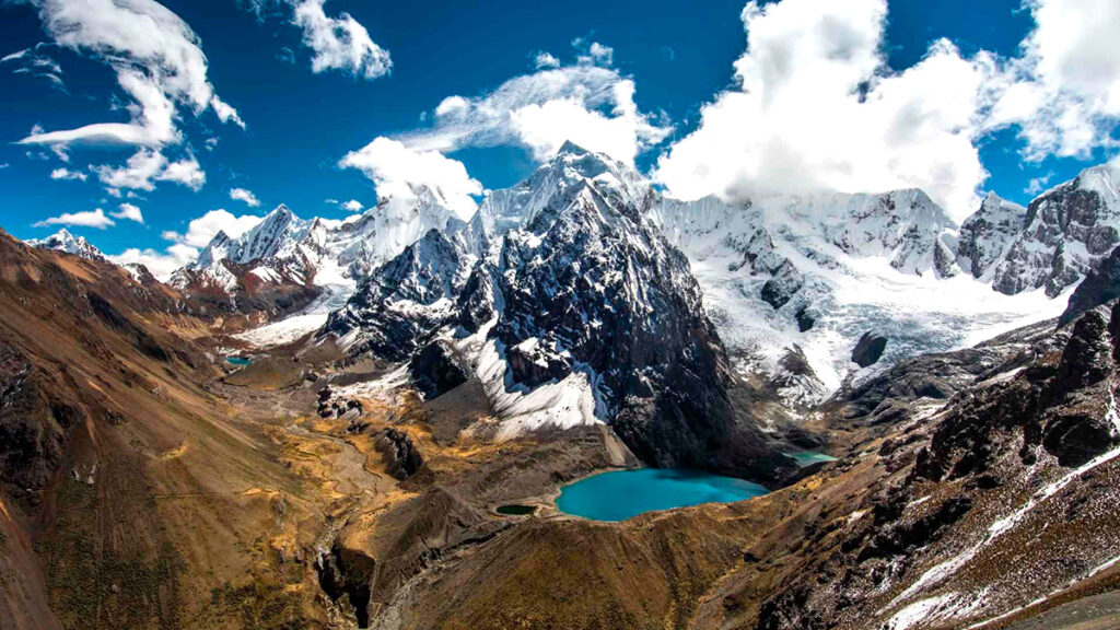 Picos nevados de la cordillera blanca, rodeados de montañas, bajo un cielo azul parcialmente nublado y en las faldas, una laguna turquesa