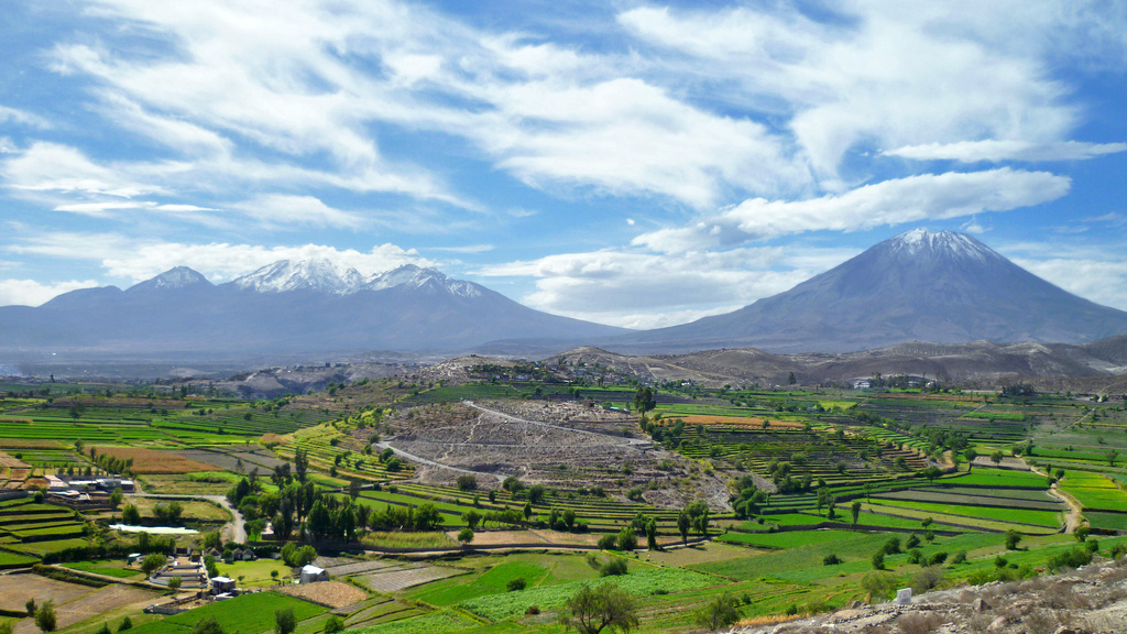 Vista panorámica del volcán isti con el paisaje agrícola de arequipa en primer plano, bajo un cielo parcialmente nublado