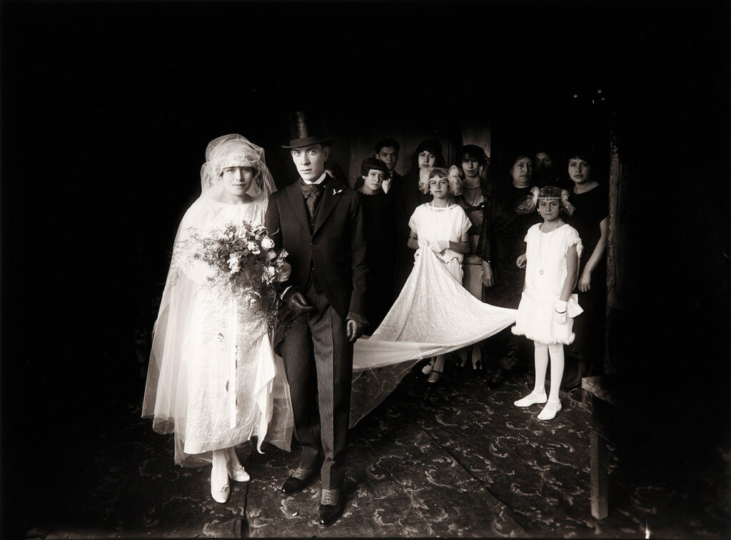 Fotografía antigua en blanco y negro de una boda, tomada por Martín Chambi, con los novios y el cortejo sobre un fondo oscuro