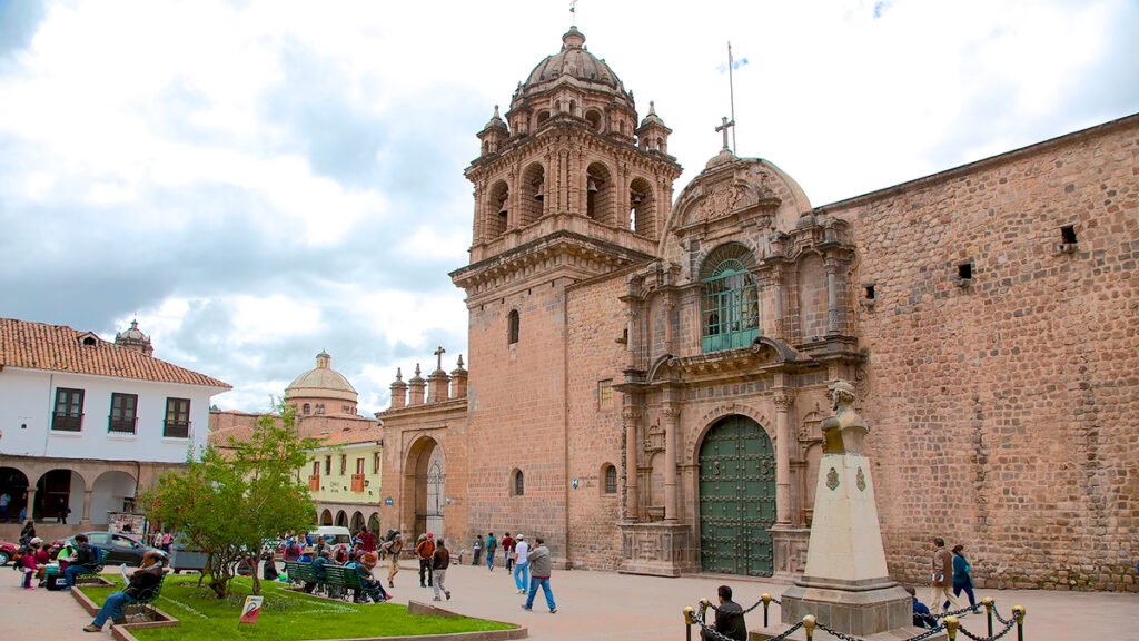 Fachada de la iglesia de La Merced en Cusco con visitantes en la plaza frontal y cielo parcialmente nublado