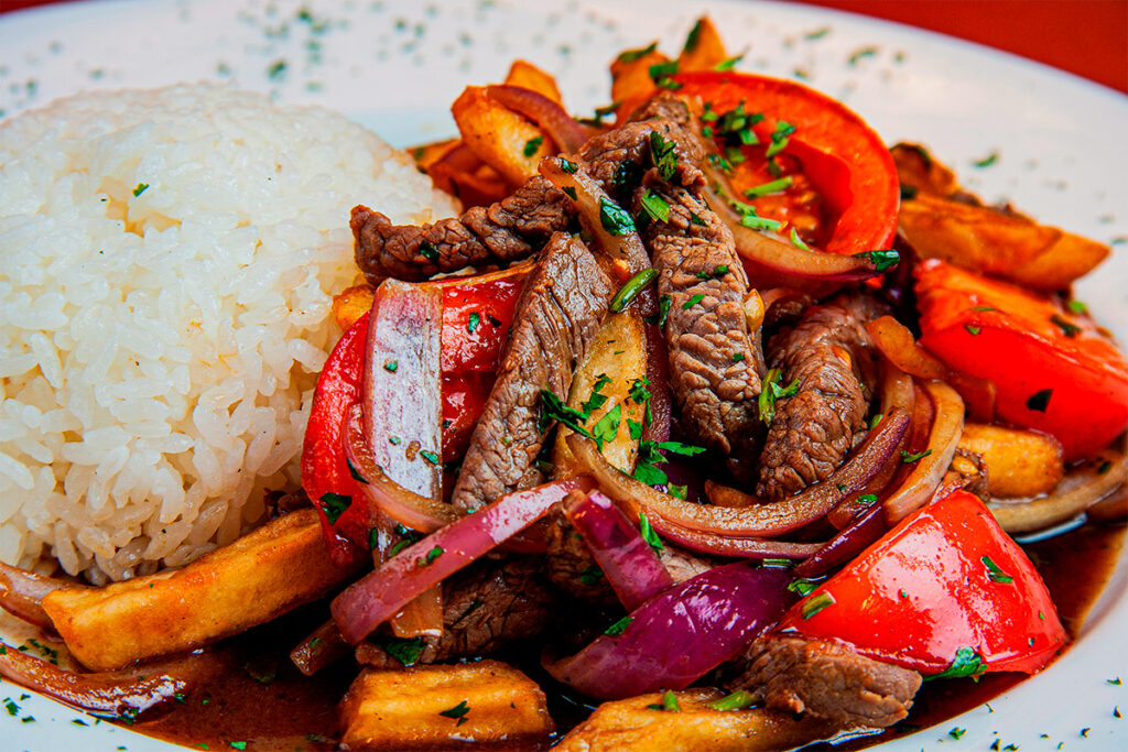 Plato de lomo saltado peruano servido con arroz blanco, cebolla morada, tomate y papas fritas