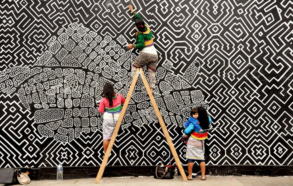 Tres mujeres pintando un mural, utilizan los patrones y símbolos del diseño kené