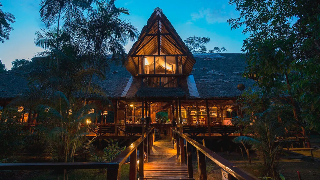 Vista nocturna del refugio amazonas, lodge ecológico rodeado de vegetación en la reserva tambopata, iluminado con luces cálidas entre los árboles