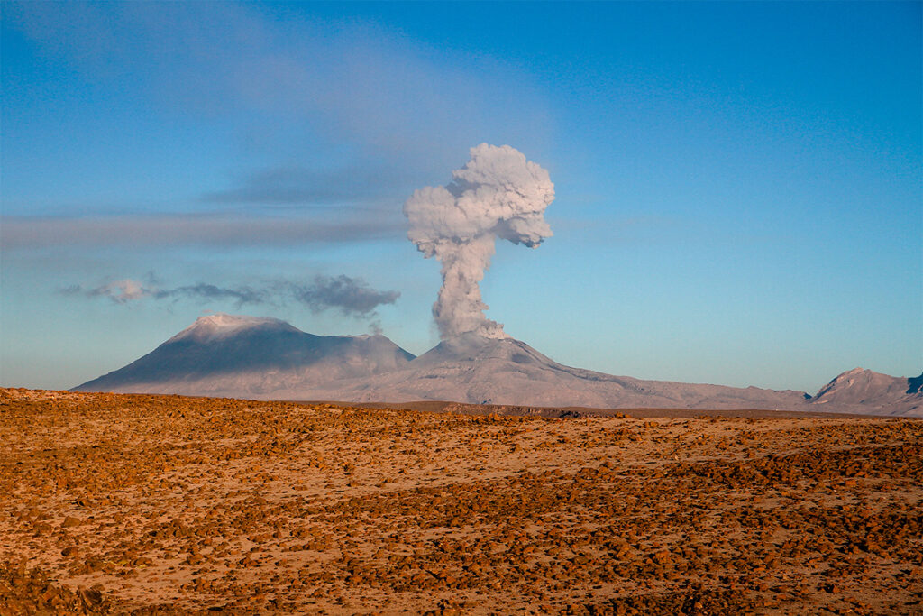 Columna de ceniza elevándose desde un volcán activo del sur del perú, vista desde una planicie bajo el cielo despejado