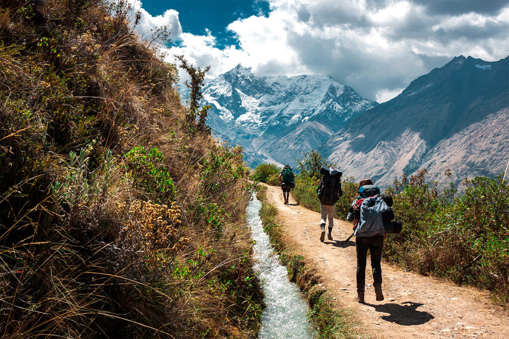 Senderistas caminando por una ruta de montaña hacia el nevado salkantay, rodeados de montañas y valles andinos en Perú