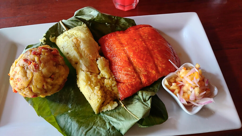 Tacacho con cecina y ají de cocona servidos sobre hojas de bijao, acompañados de chorizo amazónico y guarnición tradicional en plato amazónico peruano