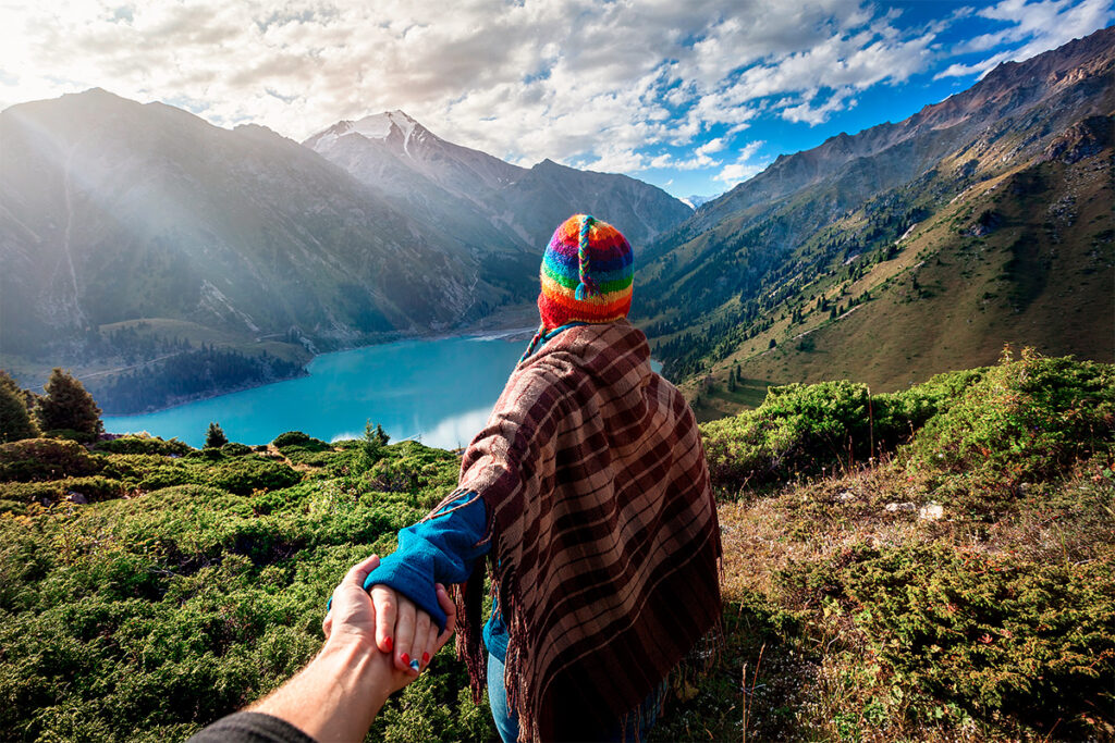 Un viajero en la montaña es guiado de la mano, al tiempo que contempla una laguna andina en Pe´ru bajo un cielo despejado