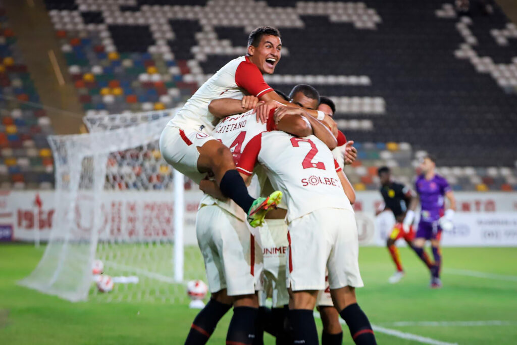 Futbolistas de Universitario de Deportes abrazándose en grupo tras marcar un gol, con las gradas del Estadio Monumental de fondo.