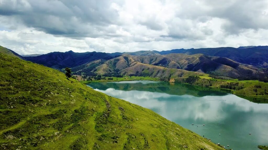 Montañas llenas de verdor acompañadas del reflejo del cielo nuboso en las aguas de una laguna, en el Valle del Mantaro, región de Junín
