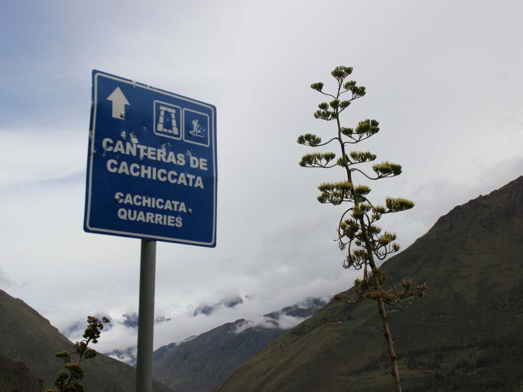 Letrero anunciando el camino hacia las canteras de Cachicata, con un fondo de montañas y niebla