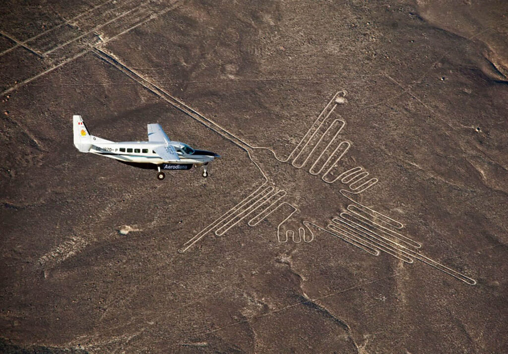 Avioneta sobrevolando las Líneas de Nazca, con vista aérea del geoglifo del colibrí en el desierto de Ica, Perú