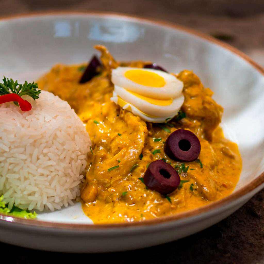 Plato de ají de gallina servido con arroz blanco, huevo duro en rodajas y aceitunas negras sobre vajilla moderna