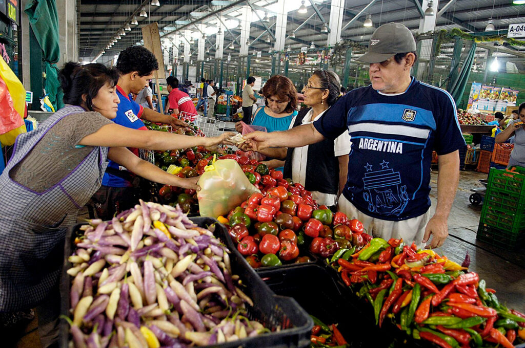 Personas comprando ajíes peruanos en un mercado tradicional, con variedades frescas expuestas sobre mesas de madera