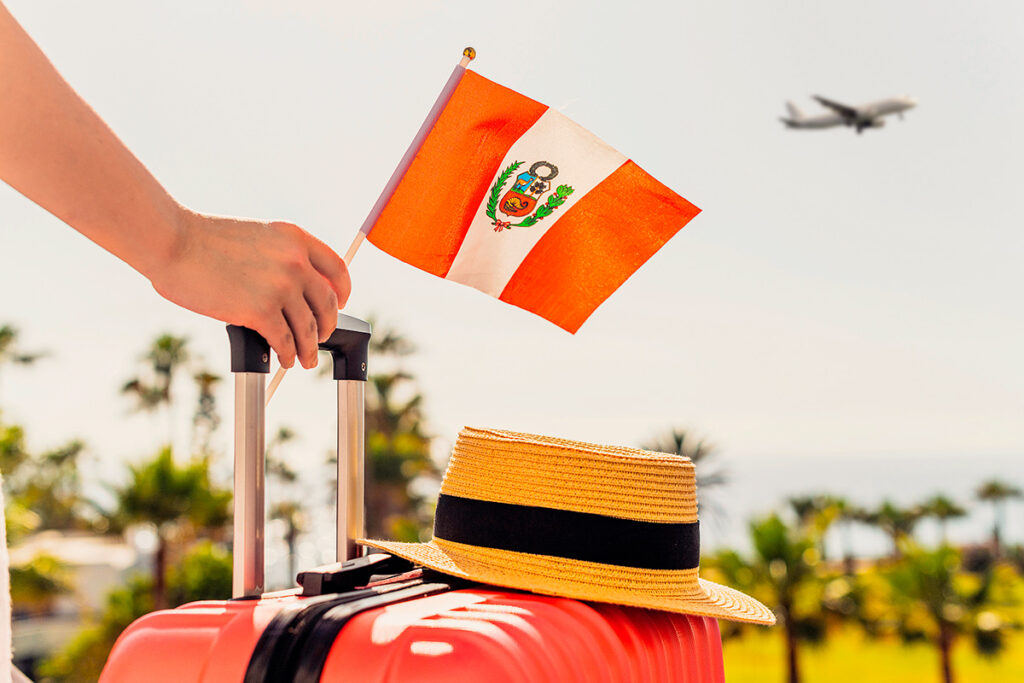 Persona sosteniendo una bandera del Perú sobre una maleta lista para viajar, con sombrero de paja y un avión despegando al fondo, símbolo del inicio de un viaje bien organizado