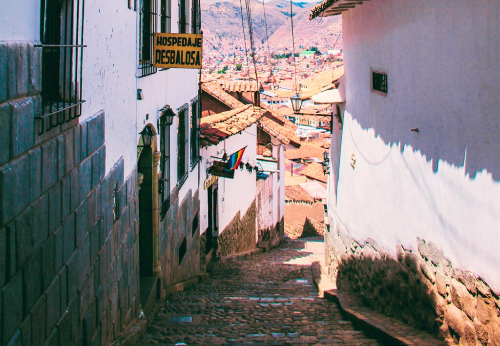 Vista descendente de la Calle Resbalosa en Cusco, con casas coloniales, muros de piedra y tejados tradicionales hacia el fondo del centro histórico de Cusco