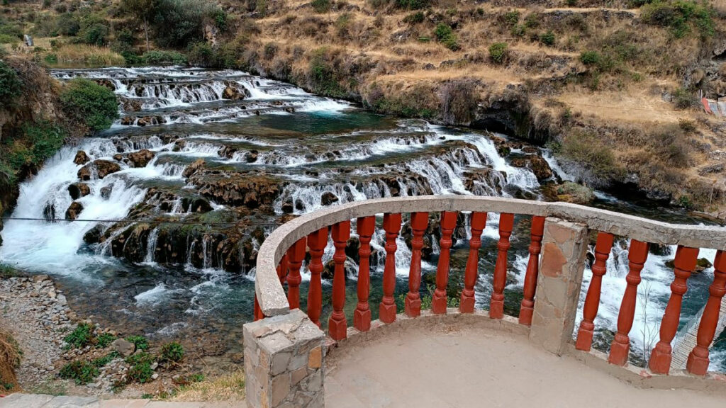 Vista de las Cascadas de Cabracancha en Huancaya desde un mirador con baranda, mostrando pozas escalonadas y agua cristalina