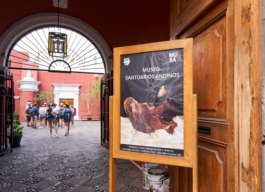 Entrada del Museo Santuarios Andinos en Arequipa, con afiche visible y visitantes ingresando al recinto