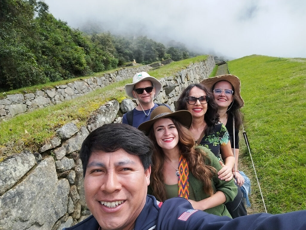 Guía turístico local sonriendo con un grupo de viajeros en un sitio arqueológico andino simbolizando la cercanía cultural y el puente humano que une al visitante con el Perú auténtico