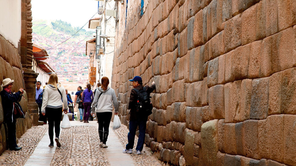 Turistas caminando por la calle Hatunrumiyoc, junto a los muros incaicos de piedra perfectamente ensamblada en el centro histórico del Cusco