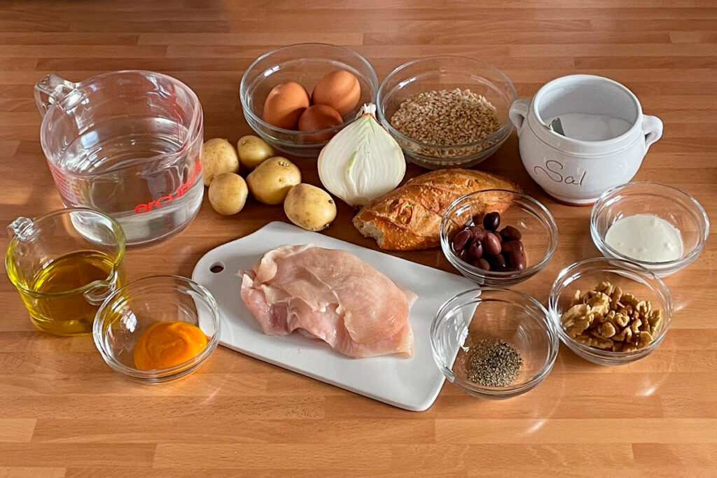 Mesa con ingredientes para preparar ají de gallina, incluyendo pollo crudo, ají amarillo, pecanas, leche, papas, huevos, cebolla y aceite