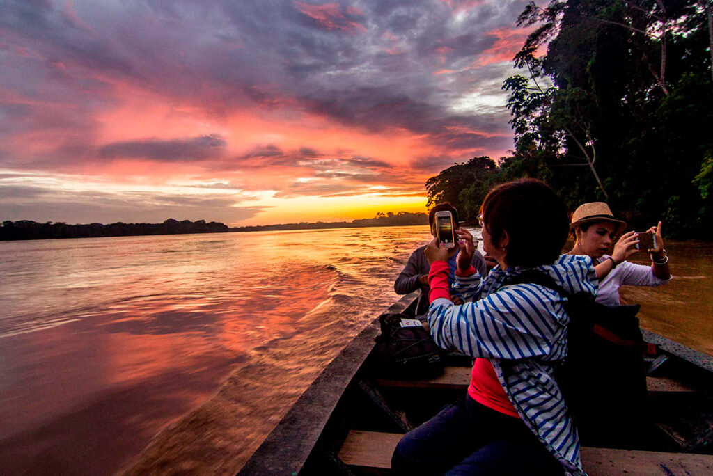 Viajeros fotografiando el atardecer amazónico en canoa sobre un río en Tambopata
