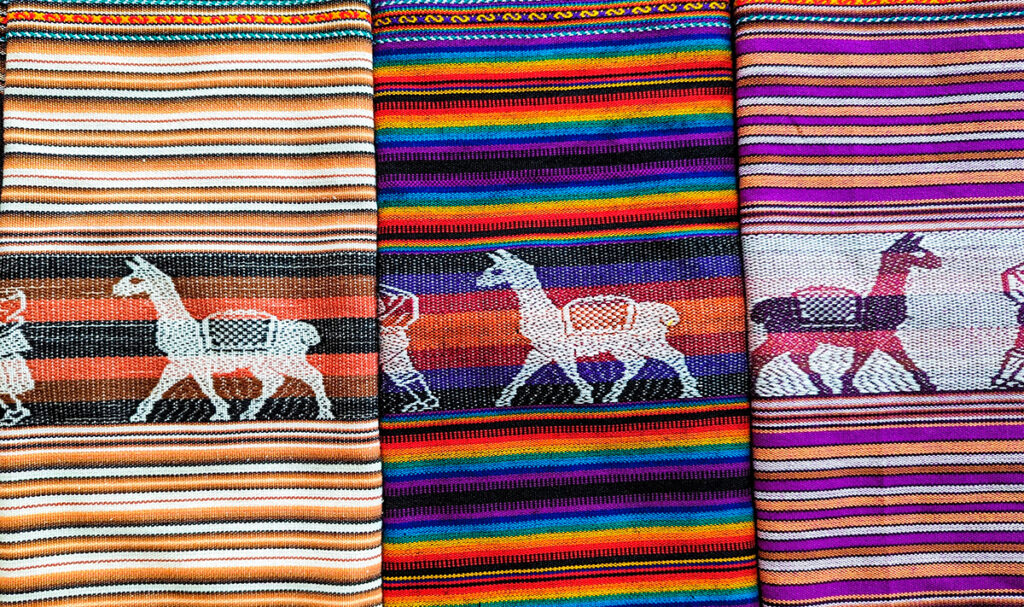 Tejidos andinos con figuras de llamas, usados en contextos rituales y turísticos como expresión de la espiritualidad ancestral