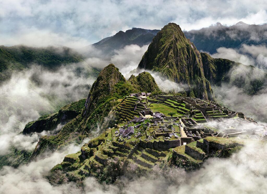 Vista panorámica de Machu Picchu entre la niebla, con terrazas verdes y templos de piedra rodeados de montañas andinas