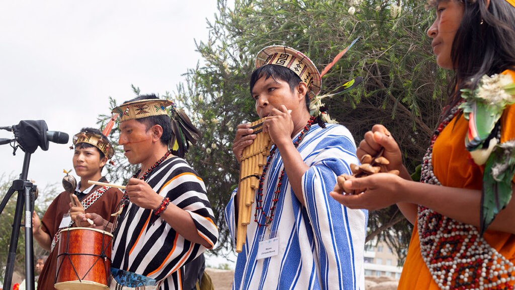 Músicos indígenas amazónicos interpretando música tradicional con tambores, antaras y vestimenta ceremonial