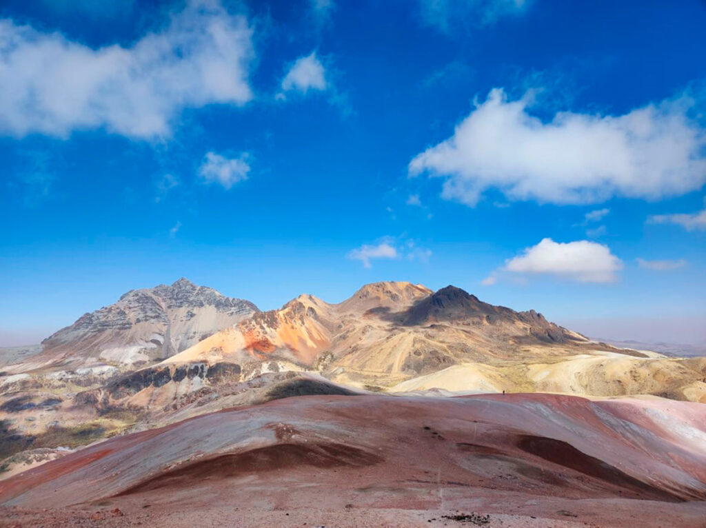 Montaña de colores Puka Puncho en Huachocolpa, Huancavelica, con laderas rojizas bajo cielo despejado